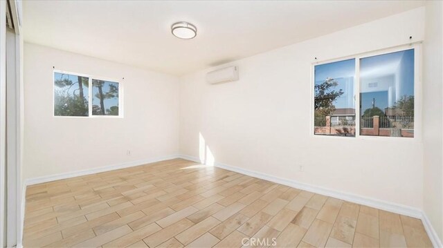 empty room with a healthy amount of sunlight, a wall mounted air conditioner, and light hardwood / wood-style floors