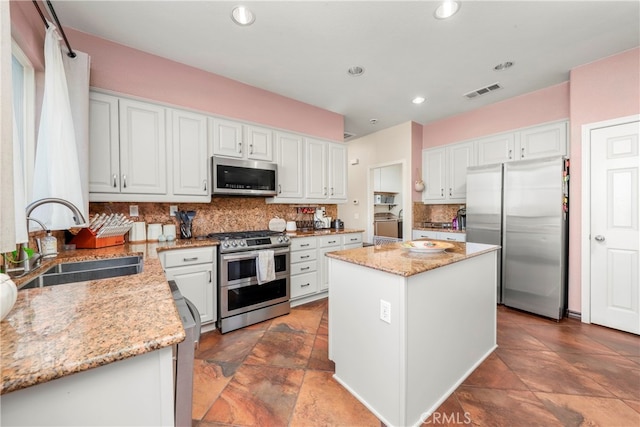 kitchen with stainless steel appliances, sink, white cabinetry, and a kitchen island