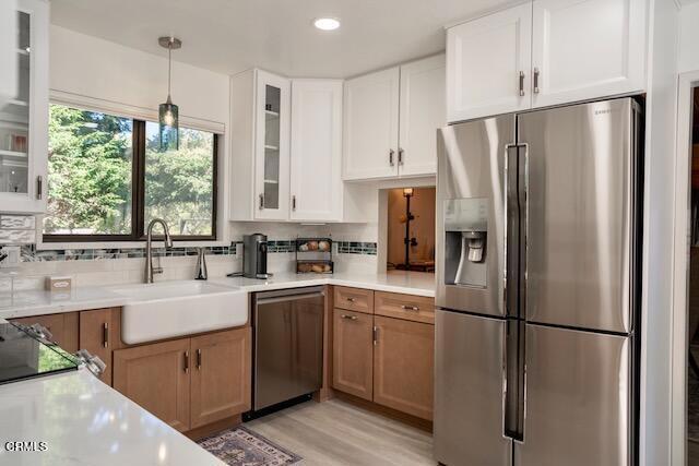 kitchen with sink, decorative light fixtures, appliances with stainless steel finishes, light hardwood / wood-style floors, and white cabinets