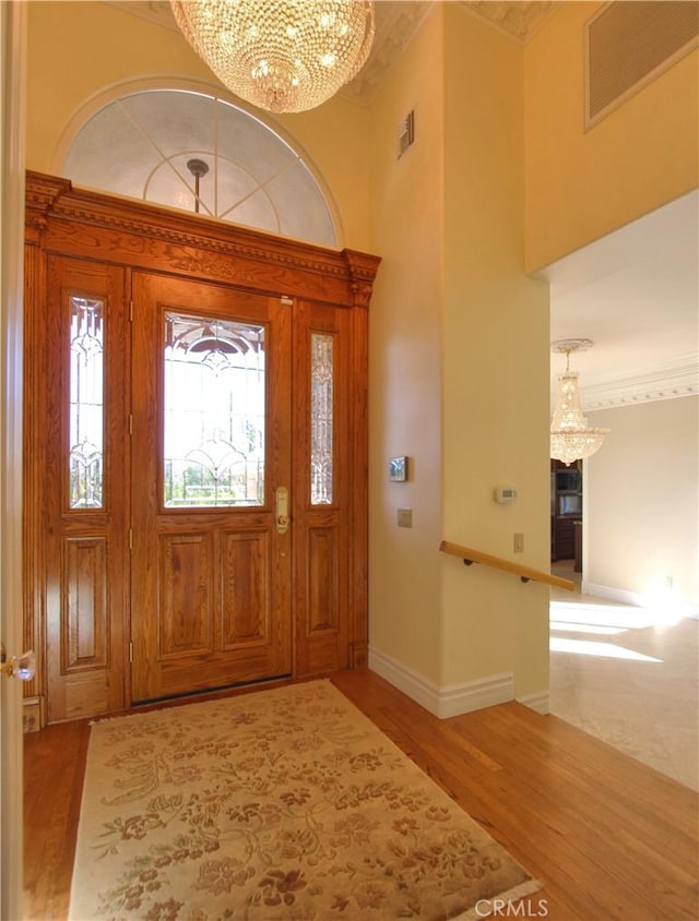 foyer entrance with a chandelier, wood-type flooring, and crown molding