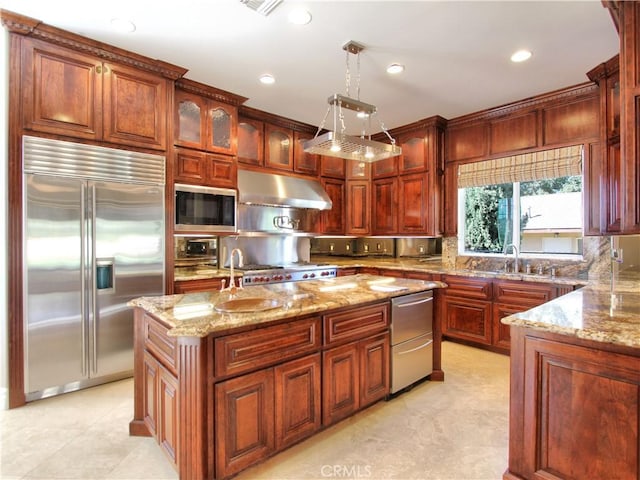 kitchen featuring light stone countertops, sink, built in appliances, a center island, and hanging light fixtures