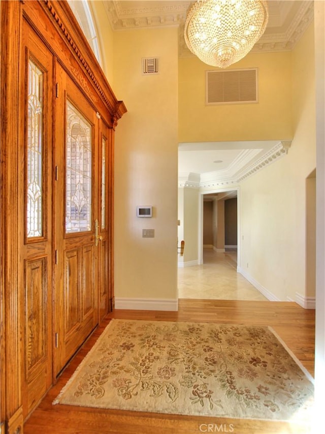 foyer with crown molding, a chandelier, and light wood-type flooring