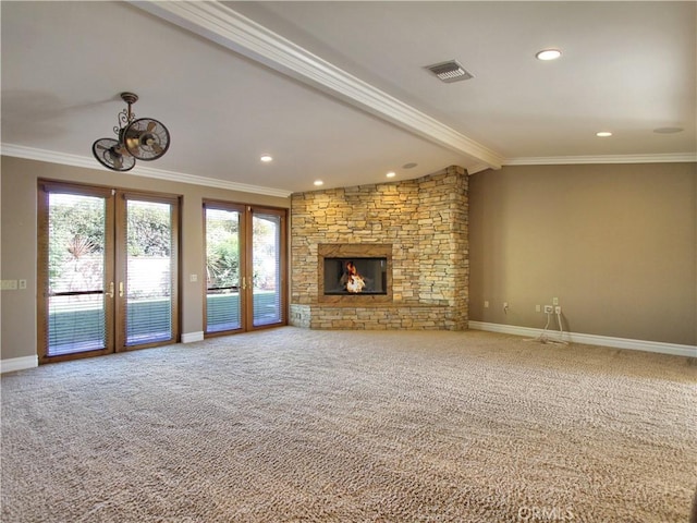 unfurnished living room with french doors, a stone fireplace, beamed ceiling, crown molding, and carpet