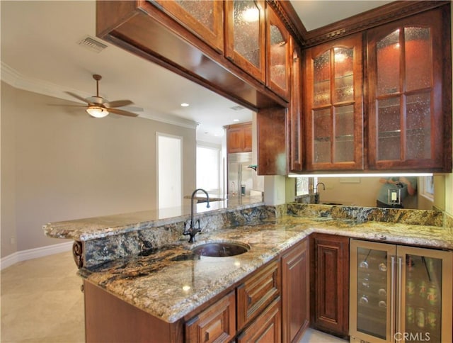 kitchen featuring kitchen peninsula, light stone countertops, ceiling fan, beverage cooler, and sink