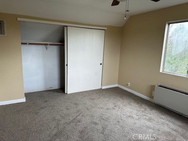 unfurnished bedroom with carpet flooring, radiator, ceiling fan, a closet, and lofted ceiling