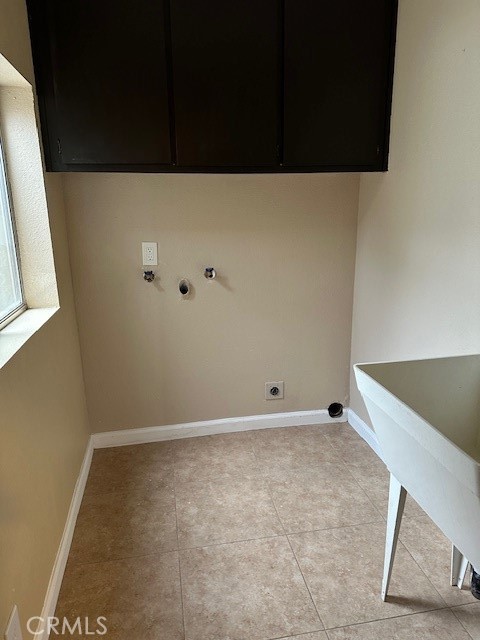 clothes washing area with gas dryer hookup, cabinets, light tile patterned floors, and electric dryer hookup