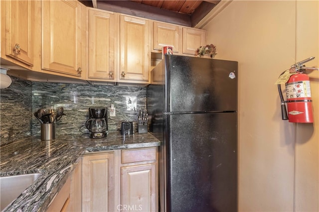 kitchen featuring black fridge, dark stone counters, light brown cabinets, and tasteful backsplash