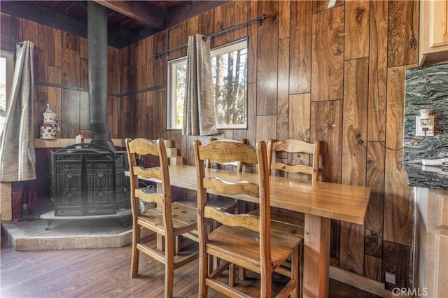 dining area with wood-type flooring, beamed ceiling, wood walls, and a wood stove