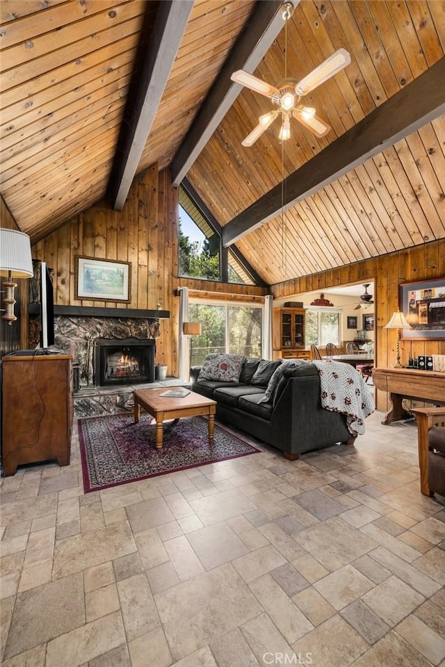 living room with ceiling fan, stone tile floors, wood walls, and lofted ceiling with beams