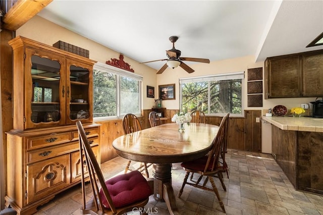 dining room featuring stone tile flooring, ceiling fan, a wainscoted wall, and wood walls