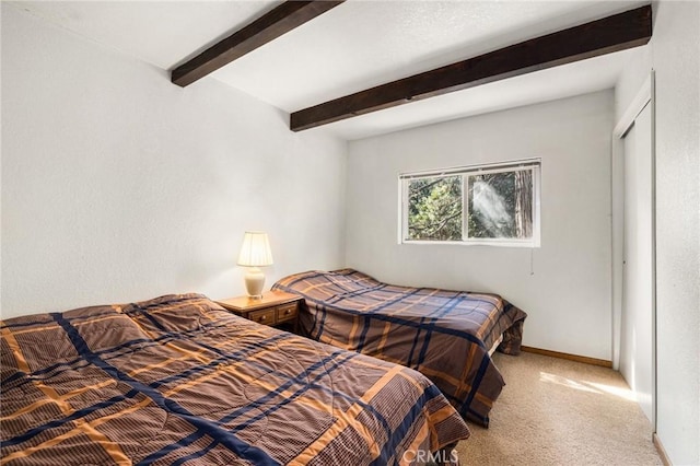 bedroom with beam ceiling, baseboards, carpet flooring, and a closet