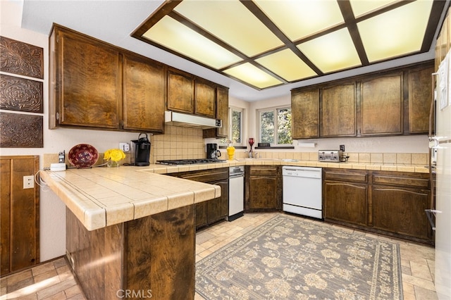 kitchen with kitchen peninsula, stainless steel gas cooktop, white dishwasher, dark brown cabinets, and tile countertops