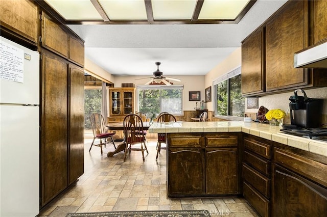 kitchen featuring a peninsula, freestanding refrigerator, stone tile flooring, and tile counters