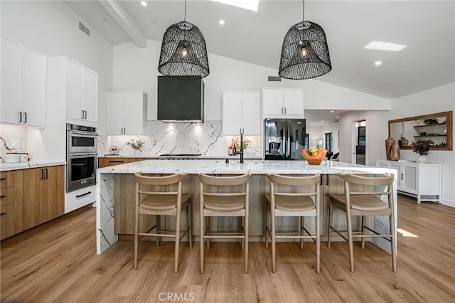 kitchen featuring light wood-style flooring, a spacious island, stainless steel appliances, decorative backsplash, and extractor fan