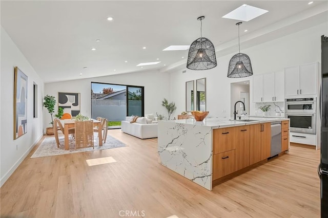 kitchen featuring pendant lighting, lofted ceiling with skylight, a large island with sink, white cabinets, and sink