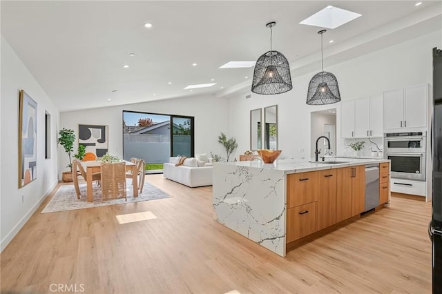 kitchen featuring a skylight, a center island with sink, light wood finished floors, and a sink