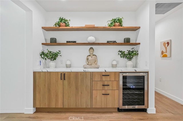 bar with visible vents, baseboards, light wood-style floors, and beverage cooler