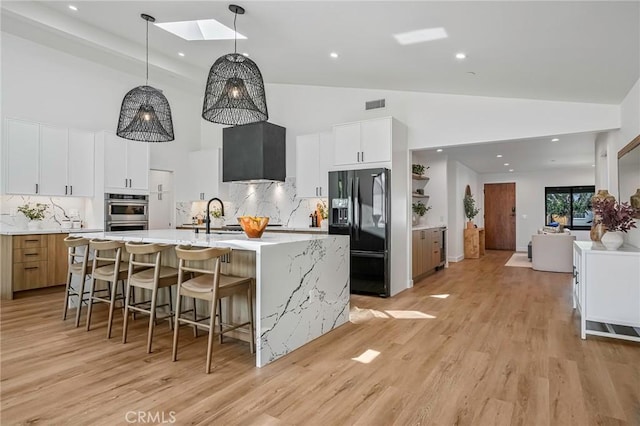 kitchen with visible vents, a kitchen bar, black fridge, a skylight, and light countertops