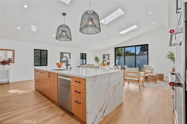 kitchen with a skylight, light wood-style flooring, a sink, stainless steel dishwasher, and open floor plan