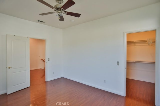 unfurnished bedroom featuring hardwood / wood-style floors, ceiling fan, a walk in closet, and a closet