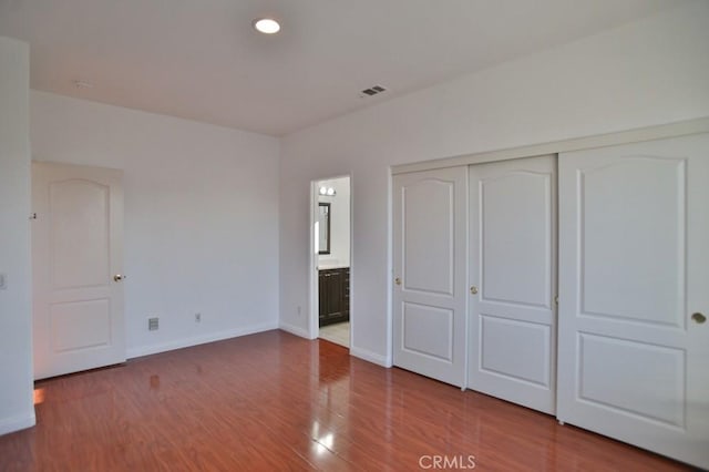 unfurnished bedroom featuring hardwood / wood-style floors, ensuite bathroom, and a closet