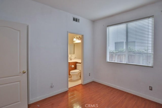 unfurnished bedroom featuring ensuite bath and light wood-type flooring