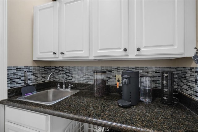 kitchen featuring backsplash, dark stone countertops, sink, and white cabinets