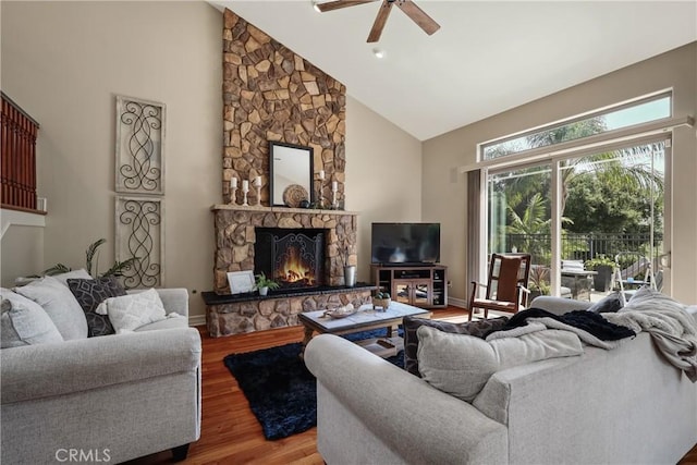 living room featuring ceiling fan, high vaulted ceiling, a stone fireplace, and hardwood / wood-style floors