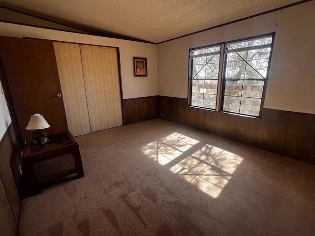 unfurnished bedroom featuring light carpet, a textured ceiling, a closet, and wood walls