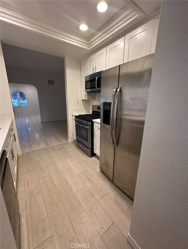 kitchen featuring stainless steel appliances, light wood-type flooring, a tray ceiling, and white cabinetry