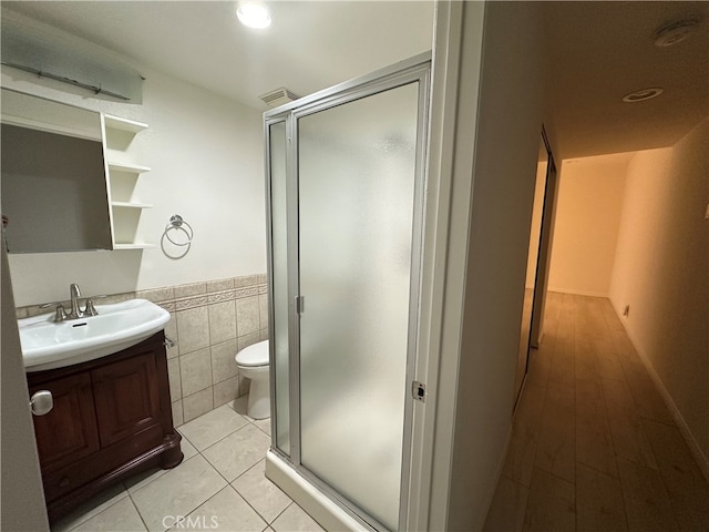 bathroom with toilet, tile patterned floors, tile walls, a shower with shower door, and vanity