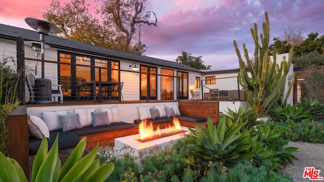 back house at dusk featuring an outdoor living space with a fire pit