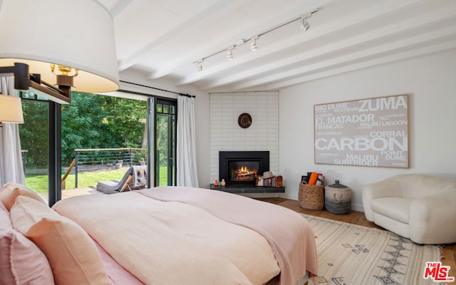 bedroom featuring hardwood / wood-style flooring, beam ceiling, access to exterior, and a fireplace