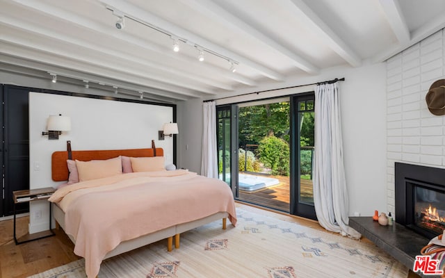 bedroom with beam ceiling, a large fireplace, light hardwood / wood-style floors, and access to outside