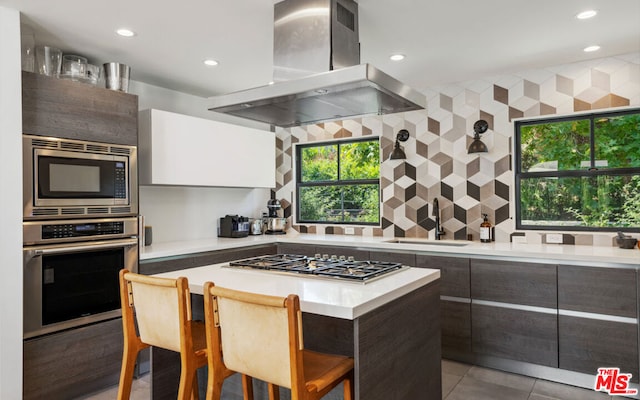 kitchen with a breakfast bar, stainless steel appliances, island range hood, sink, and a center island