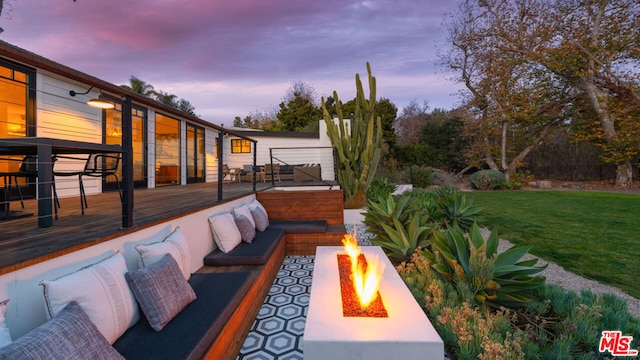 patio terrace at dusk featuring a yard, a deck, and an outdoor living space with a fire pit