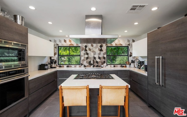 kitchen with white cabinets, a kitchen bar, island exhaust hood, and appliances with stainless steel finishes