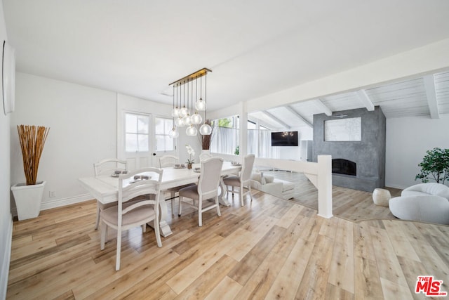 dining space featuring light hardwood / wood-style flooring, a premium fireplace, and vaulted ceiling with beams