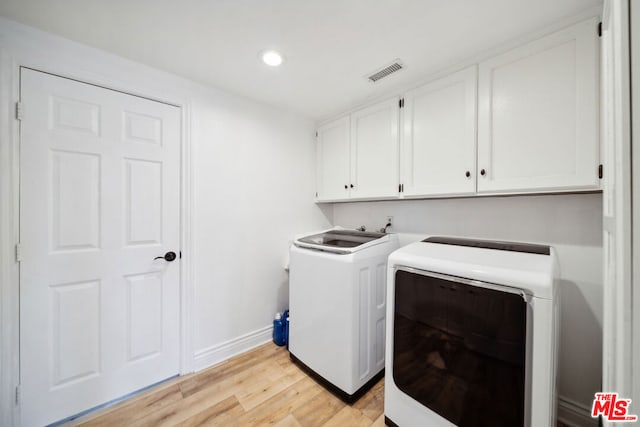 laundry room featuring washing machine and clothes dryer, cabinets, and light wood-type flooring