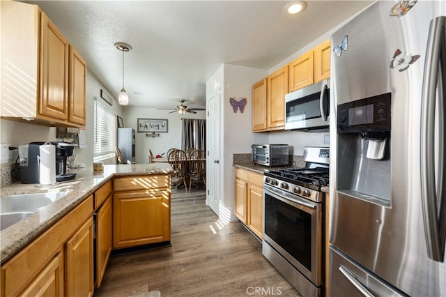 kitchen with dark wood-type flooring, stainless steel appliances, light stone countertops, pendant lighting, and ceiling fan