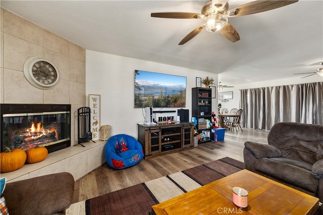 living room with wood-type flooring, a tile fireplace, and ceiling fan