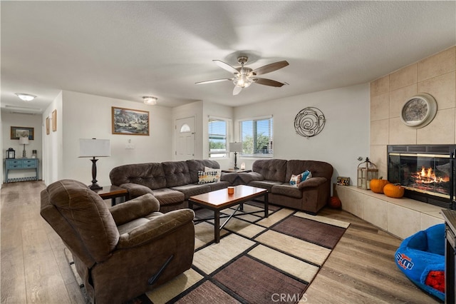 living room featuring a textured ceiling, a tile fireplace, light wood-type flooring, and ceiling fan