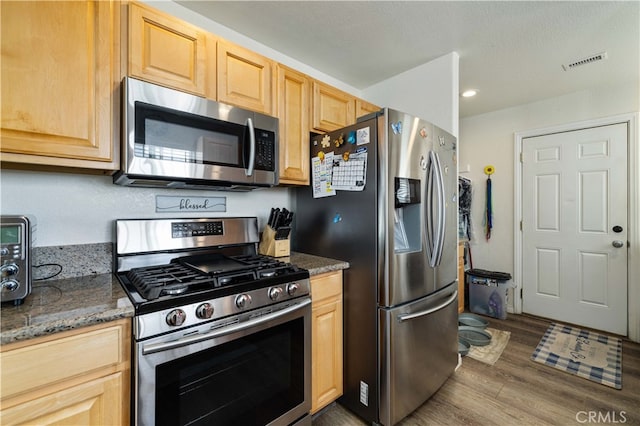 kitchen featuring appliances with stainless steel finishes, light brown cabinets, dark stone counters, and dark hardwood / wood-style flooring