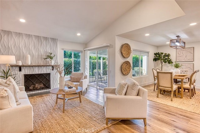 living room featuring lofted ceiling, a healthy amount of sunlight, a large fireplace, and light hardwood / wood-style flooring