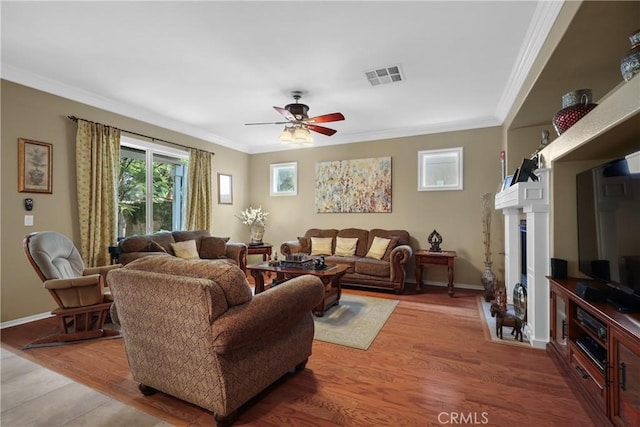 living room with ceiling fan, a fireplace, wood finished floors, visible vents, and crown molding