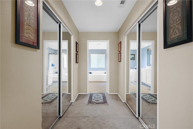 corridor featuring baseboards, light tile patterned flooring, visible vents, and light colored carpet