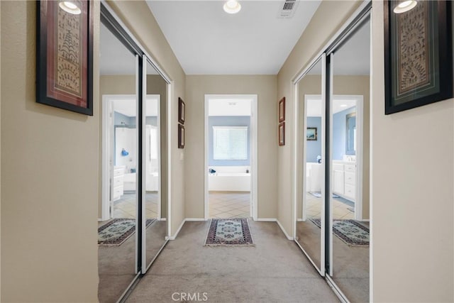 corridor with light carpet, baseboards, and visible vents