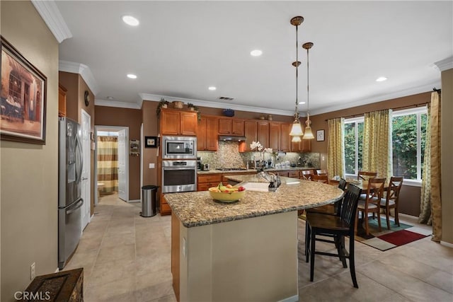 kitchen with light stone counters, brown cabinets, a center island, decorative light fixtures, and stainless steel appliances