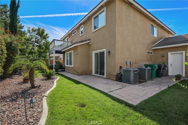 rear view of house with stucco siding, central AC unit, a balcony, and a lawn