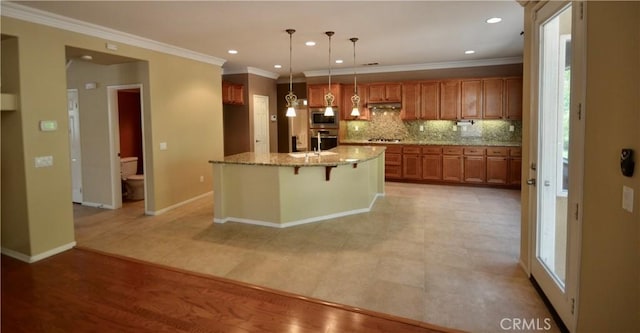 kitchen featuring light stone counters, crown molding, decorative backsplash, brown cabinetry, and hanging light fixtures